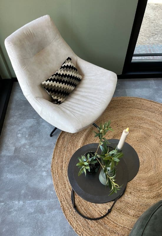 Grijze velvet fauteuil rond jute vloerkleed zwarte ronde bijzettafeltjes