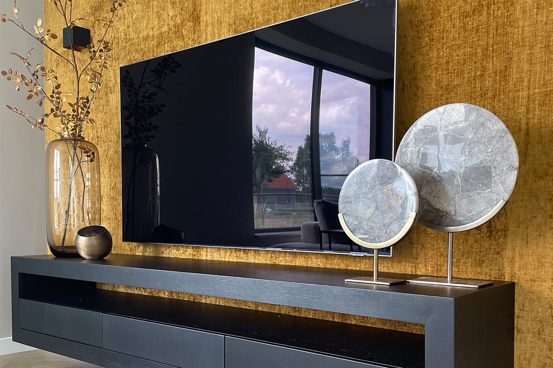 Okergeel behang zwart zwevend tv meubel grijze natuursteen ornamenten op gouden voet