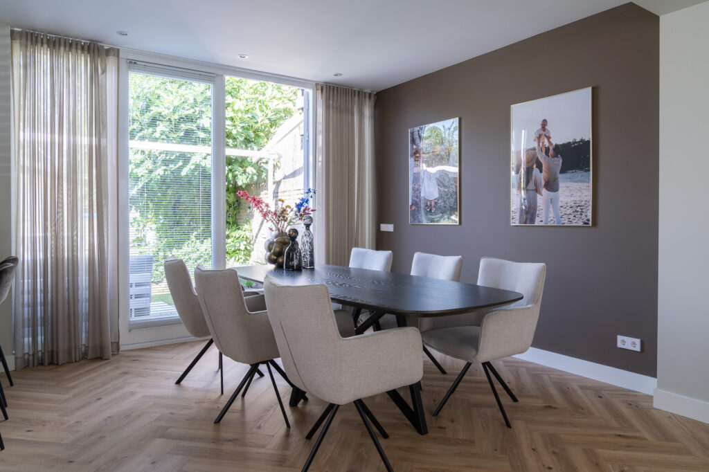 Deens ovale eettafel met beige eetkamerstoelen en bruine muurverf